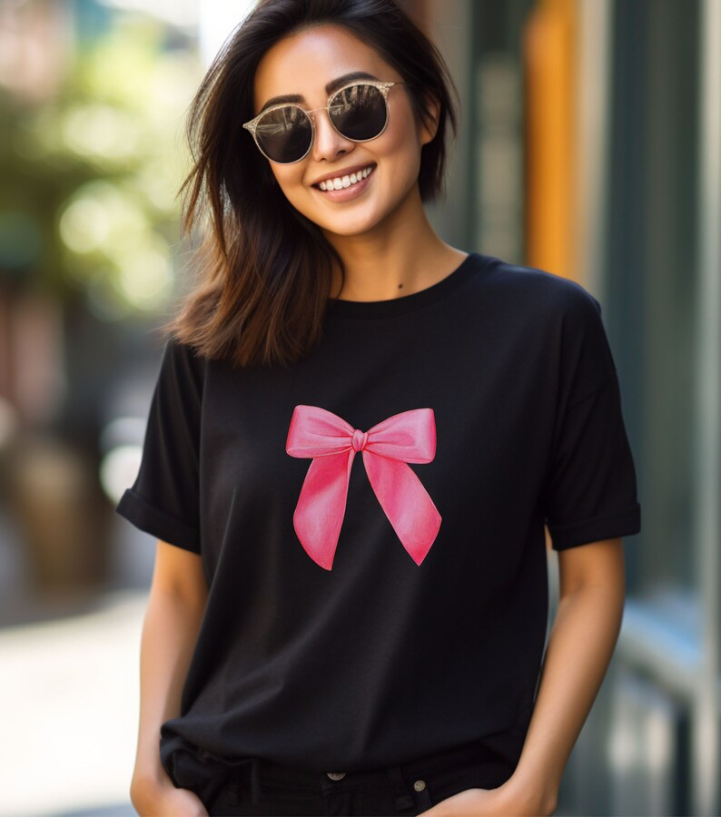 May include: A black t-shirt with a pink bow graphic on the front. The shirt has a crew neck and short sleeves.
