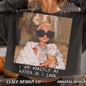 May include: A charcoal gray cropped sweatshirt featuring a graphic print of a doll with blonde hair in a high ponytail, wearing large black sunglasses, a white knit top, and a white cardigan, while holding a coffee cup with the text I AM EXACTLY AS EXTRA AS I LOOK.