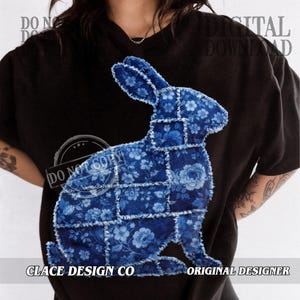 May include: Black t-shirt with a blue floral patchwork rabbit design. The rabbit is made up of different blue floral patterns, with visible stitching. The text "CLACE DESIGN CO" and "ORIGINAL DESIGNER" are printed at the bottom.