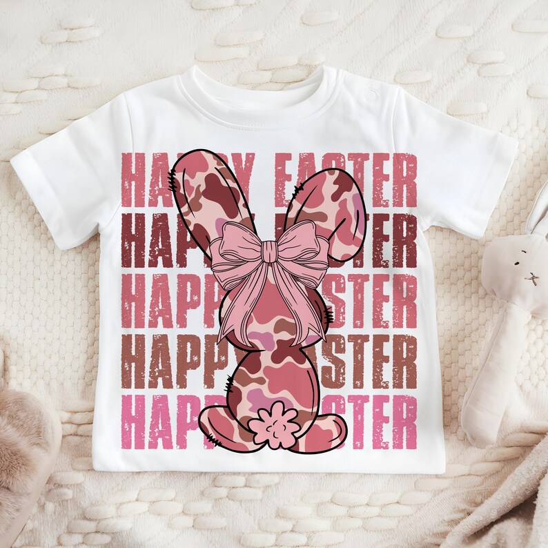 May include: White t-shirt featuring a pink and brown camouflage bunny rabbit wearing a pink bow. The shirt has the text "Happy Easter" repeated five times in pink and brown.