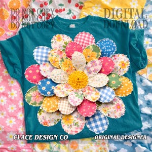 Peut inclure: T-shirt turquoise avec une grande application de fleur colorée. La fleur a des pétales de différentes couleurs et motifs, dont des pois roses, du vichy bleu et des imprimés floraux. Le centre de la fleur est jaune. Le texte sur le t-shirt indique "CLACE DESIGN CO" et "ORIGINAL DESIGNER".