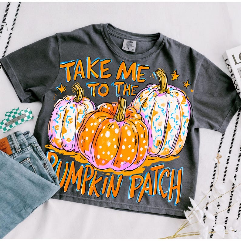 May include: A charcoal gray short-sleeve t-shirt featuring a graphic of three pumpkins with orange and white polka dots. The text reads "TAKE ME TO THE PUMPKIN PATCH" in orange lettering. The design includes small orange stars and a distressed finish.