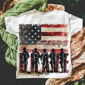 May include: White t-shirt with a distressed American flag design and the text "land of the free because of the BRAVE".