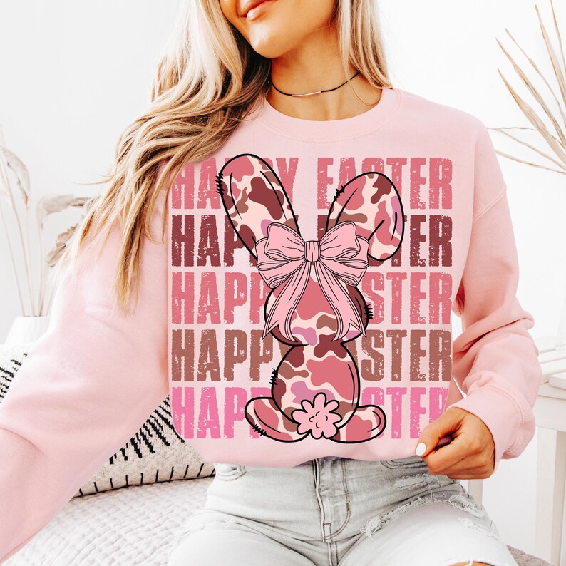 May include: Pink sweatshirt featuring a pink and brown camouflage bunny with a pink bow. The text "Happy Easter" is repeated in a distressed font on the sweatshirt.