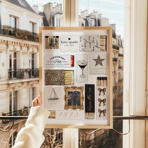 May include: A gold-framed picture with a white background and various matchboxes. The matchboxes feature a leopard print, a cocktail glass, a star, a sailboat, a photo of a couple, and the text "Enjoy the now". The matchboxes also have the text "kate spade NEW YORK", "TOBERMORY EST 1798 THE ISLE OF MULL SINGLE MALT SCOTCH WHISKY", and "1373".