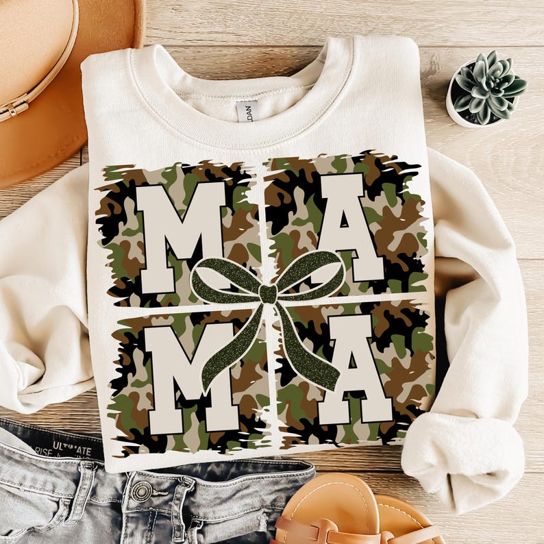 Pu&ograve; includere: Una felpa bianca con un design a stampa mimetica che scrive "MAMA" con un fiocco verde al centro.