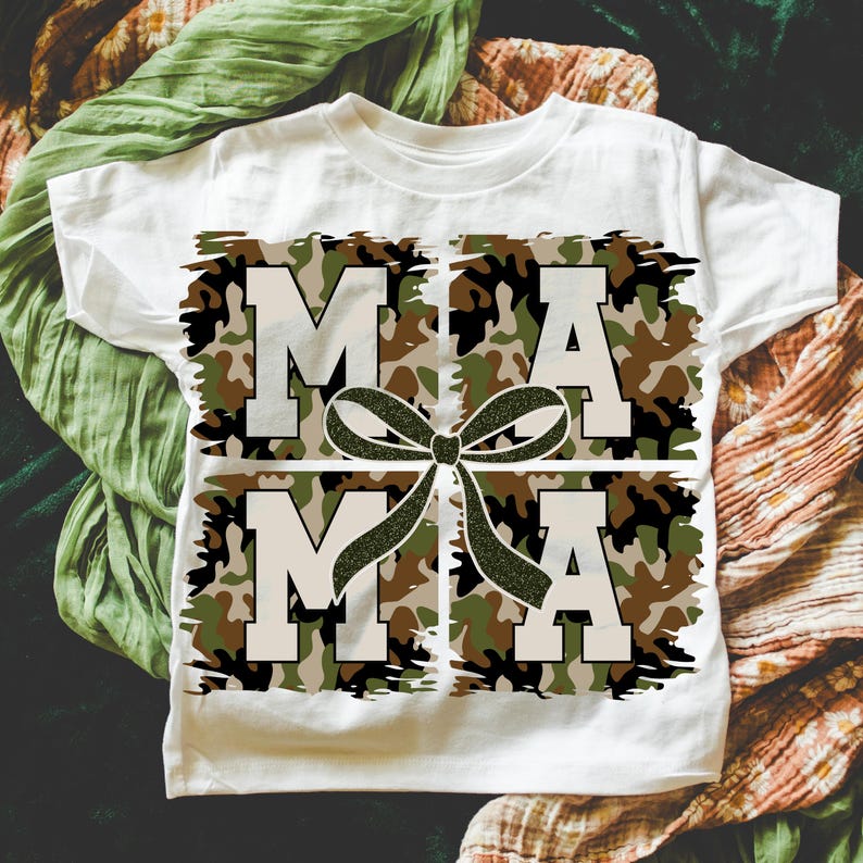 Pu&ograve; includere: Maglietta bianca con un design a fantasia mimetica che scrive "MAMA" con un fiocco verde al centro.