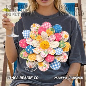 K&ouml;nnte beinhalten: Dunkelgraues T-Shirt mit einem gro&szlig;en, farbenfrohen Blumenmuster. Die Blume hat gemusterte Bl&uuml;tenbl&auml;tter in Rosa, Blau, Gelb und Gr&uuml;n. Das Shirt tr&auml;gt auch den Text "CLACE DESIGN CO" und "ORIGINAL DESIGNER".