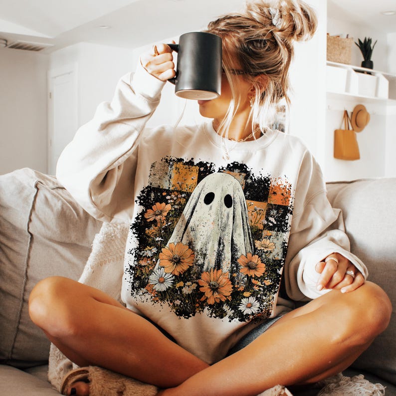 Puede incluir: Sudadera color crema con un dise&ntilde;o de fantasma con flores naranjas y blancas. El fantasma tiene dos ojos negros y est&aacute; rodeado de un arreglo floral. La sudadera es de corte holgado y adecuada para uso casual.