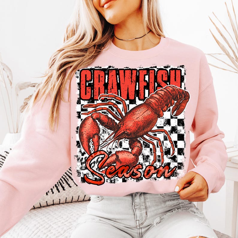 May include: Pink sweatshirt with a red crawfish graphic and the text "Crawfish Season" on a black and white checkered background.