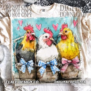 May include: Cream-colored t-shirt featuring a watercolor design of three chickens in baskets, each with a bow. The chickens are yellow, white, and black, with red combs. Pink hearts float above them. Text on the shirt reads "DIGITAL DOWNLOAD".