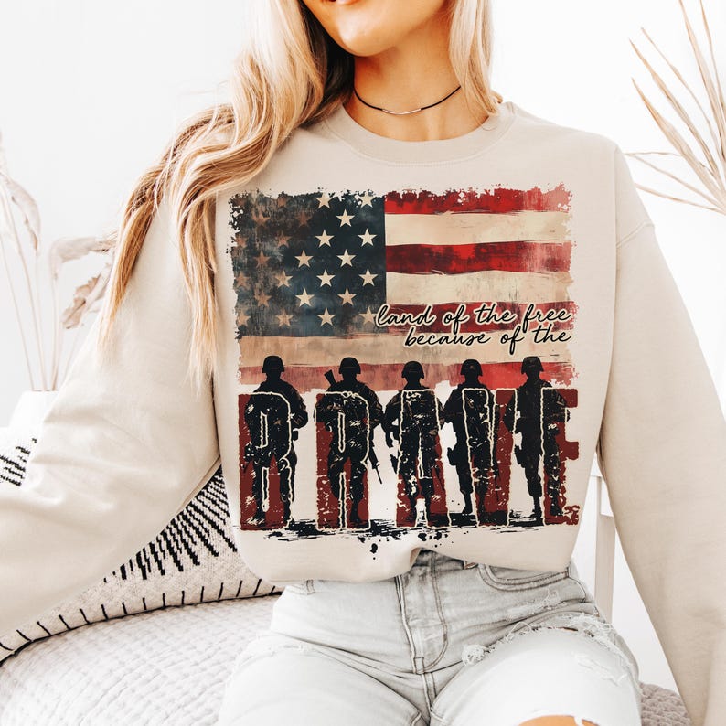 May include: A beige sweatshirt with a distressed American flag design and the text "land of the free because of the BRAVE".