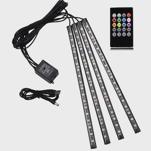 May include: A set of four thin, flexible LED light strips with black wiring, a small rectangular IR controller box, a USB power cable, and a black remote control featuring multiple colored buttons for adjusting light settings and modes.