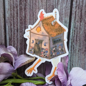 May include: A sticker of a whimsical house with a stone exterior and a red tiled roof. The house has a chimney and a small door. The house is on chicken legs and has a rooster's comb on top.