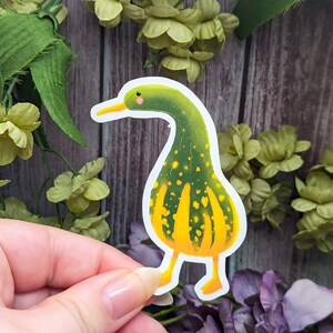 May include: A green and yellow gourd-shaped sticker with a duck head and feet. The sticker is on a white background.