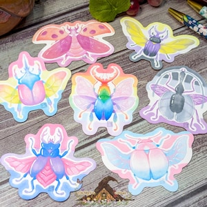 Può includere: Una collezione di sette adesivi fustellati raffiguranti varie illustrazioni di coleotteri in colori vivaci, tra cui sfumature di rosa, giallo, blu e arcobaleno. Ogni adesivo mostra una forma di insetto unica con ali e zampe dettagliate.