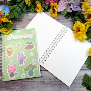 May include: A spiral-bound notebook and a sticker collection book with a green cover featuring cartoon characters and the text "My Growing Sticker Collection." The background includes a wooden surface and colourful flowers.