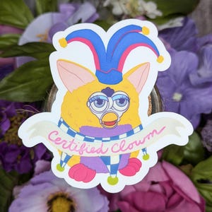 May include: A yellow and purple fuzzy creature wearing a blue and pink jester hat with a white banner that says "Certified Clown".