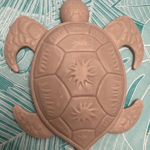 May include: A gray ceramic turtle sculpture with a detailed shell design. The shell has a sunburst pattern on each of the segments.