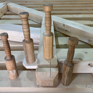 May include: Four wooden mallets of varying sizes, with a natural wood finish, are arranged on a wooden surface. The mallets are used for woodworking and have a smooth, rounded head.