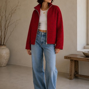 Puede incluir: Una chaqueta con cremallera de cuadros rojos y negros con cuello alto, usada sobre una camiseta sin mangas blanca y pantalones vaqueros anchos de color azul claro. La chaqueta presenta un patr&oacute;n de rejilla, mangas largas y cremallera plateada.