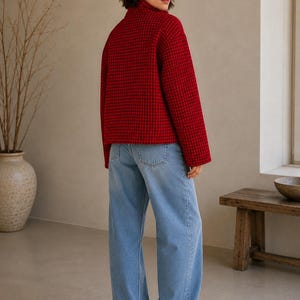 Puede incluir: Una chaqueta roja con patr&oacute;n de cuadr&iacute;cula negra y cuello alto, combinada con pantalones vaqueros de mezclilla azul claro y zapatillas blancas. La chaqueta presenta mangas largas y un dobladillo recto, mientras que los vaqueros tienen un corte holgado.