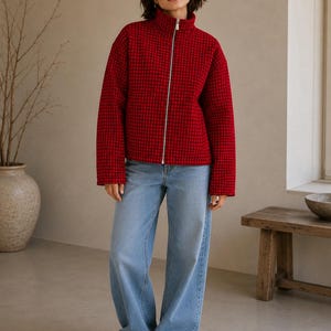 Puede incluir: Una chaqueta roja con un patr&oacute;n de cuadr&iacute;cula negra, cuello alto y cremallera plateada de cuerpo entero, combinada con pantalones vaqueros de mezclilla azul claro y zapatillas blancas. La chaqueta tiene mangas largas y un corte estructurado.