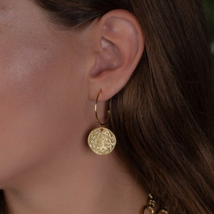 Gold hoop earrings with hammered coin charms. Delicate half-hoop gold earring with a gold coin on it.