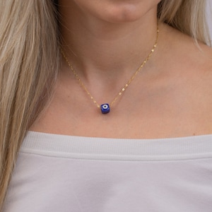 A gold thin chain with a blue evil eye charm in a cube shape. Delicate and minimal necklace, Greek evil eye that gives protection.An everyday necklace that can be layered with all the jewelry.