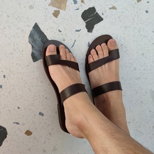 May include: A pair of brown leather sandals with two straps across the foot. The sandals have a simple design and are ideal for warm weather.