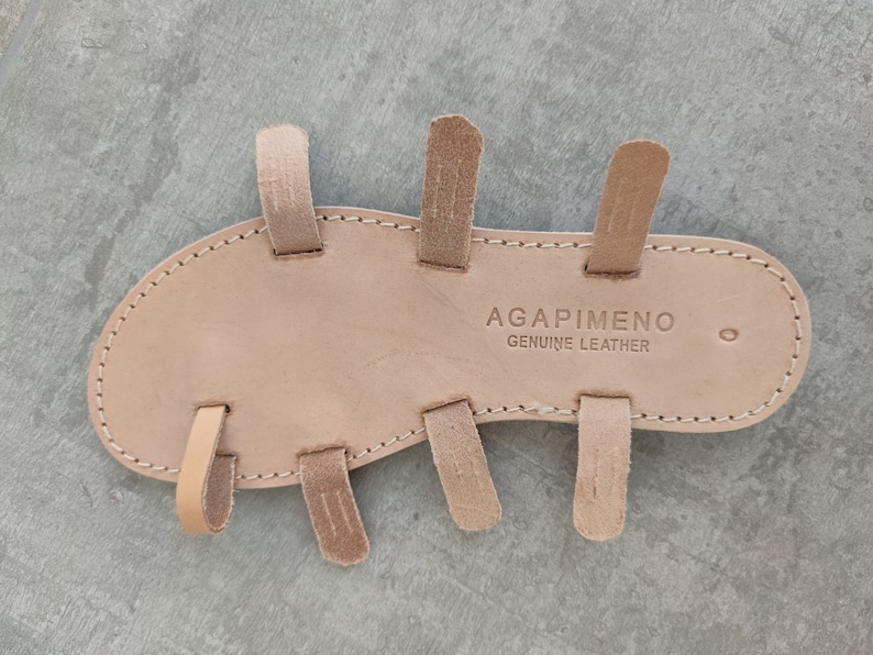 May include: The underside of a light brown leather sandal with multiple straps. The sandal is labelled "AGAPIMENO GENUINE LEATHER".