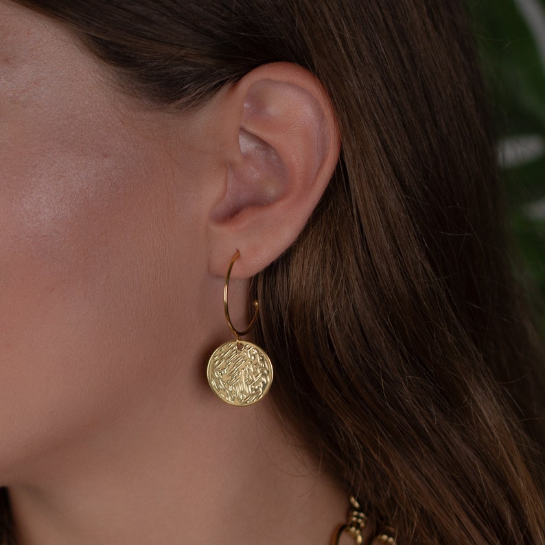 Gold hoop earrings with hammered coin charms. Delicate half-hoop gold earring with a gold coin on it.