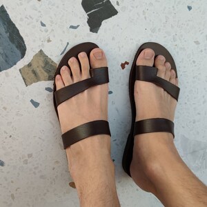 May include: A pair of brown leather sandals with two straps across the foot. The sandals have a simple design and are made of high-quality leather.