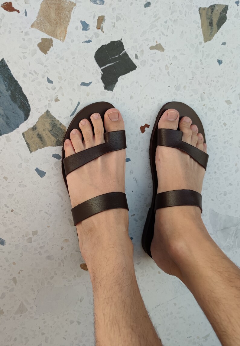 May include: A pair of brown leather sandals with two straps across the foot. The sandals have a simple design and are made of high-quality leather.