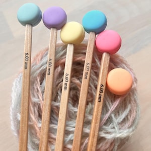 Peut inclure: Six aiguilles à tricoter en bois avec des embouts en forme de macaron colorés. Les aiguilles mesurent 6,00 mm et sont disposées en éventail. Les embouts en forme de macaron sont de couleur bleue, violette, jaune, rose et orange.