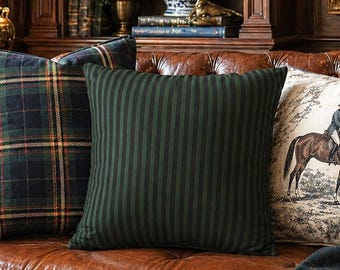 May include: A brown leather sofa featuring three decorative pillows: one with a dark green and blue plaid pattern, one with dark green vertical stripes, and one with a cream-colored fabric depicting a person riding a brown horse in a landscape.