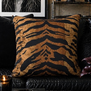 May include: A square throw pillow featuring a prominent tiger stripe pattern in shades of deep black and warm, textured brown. The fabric displays a soft, velvet-like appearance with a repeating animal print design centered on the cushion.