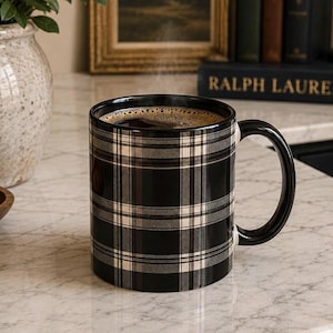 May include: A ceramic mug featuring a black, white, and gray plaid pattern. The mug has a solid black handle and is filled with dark coffee. The exterior surface of the mug displays a consistent grid-like tartan design with intersecting lines.
