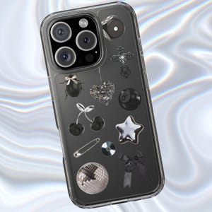 Puede incluir: Funda transparente para teléfono con fondo negro y varios amuletos. Los amuletos incluyen un escarabajo, un corazón, cerezas, un imperdible, una estrella, una bola de discoteca, una cruz, una bola ocho y un lazo. La funda tiene un borde transparente.