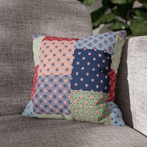 May include: Square patchwork cushion featuring floral and polka dot patterns in red, pink, blue, green, and purple. The cushion is placed on a grey upholstered sofa.
