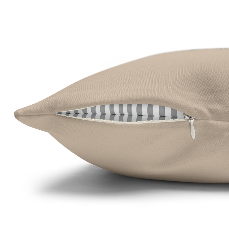 May include: A solid beige throw pillow featuring a hidden zipper closure along the side. The interior fabric visible through the slightly open zipper displays a pattern of alternating vertical white and grey stripes on a neutral background.