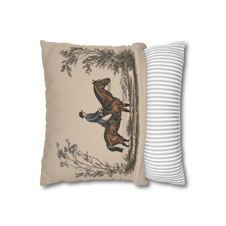 May include: A rectangular throw pillow featuring a beige front panel with a detailed illustration of a person riding a brown horse through a wooded landscape. The side panel of the pillow displays a pattern of thin, alternating white and gray stripes.