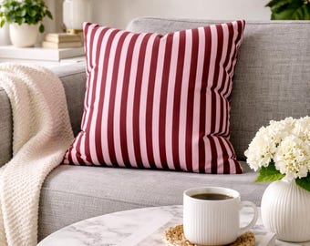 May include: A square throw pillow featuring vertical stripes in alternating shades of deep burgundy and soft light pink. The pillow is made of fabric and has a plump, filled appearance, showcasing a consistent striped pattern across its surface.