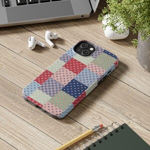 Puede incluir: Funda de teléfono con diseño de patchwork colorido. El diseño presenta cuadrados rojos, azules y verdes, con patrones florales y de puntos. Se encuentra sobre una superficie de madera con un portátil, auriculares y un cuaderno.