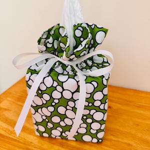 May include: A fabric tissue box cover with a green and white bubble pattern. The box is tied with a white ribbon. White tissues are visible at the top of the box.