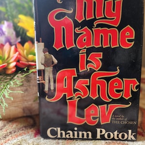 May include: A hardcover book titled "My Name is Asher Lev" by Chaim Potok. The cover is black with red lettering and features an illustration of a person painting. The book is a novel by the author of "The Chosen".
