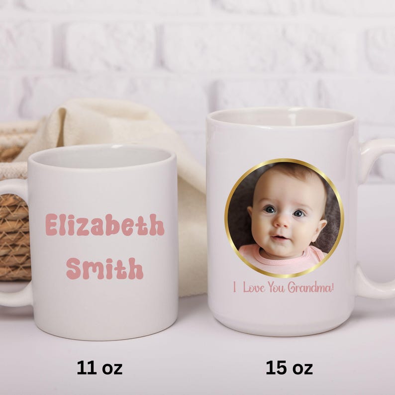May include: Two white ceramic mugs, one 11 oz and one 15 oz. The 11 oz mug features the pink text Elizabeth Smith. The 15 oz mug displays a circular photograph of a baby framed in gold with the pink text I Love You Grandma below the image.