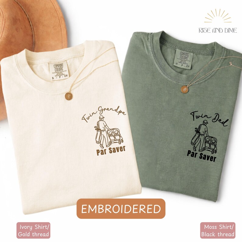 May include: Two t-shirts, one ivory and one moss green, with embroidered golf-themed designs. The ivory shirt features "Twin Grandpa" and the moss green shirt says "Twin Dad". Both shirts have a golfer graphic and the words "Par Saver".