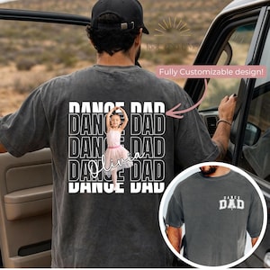 May include: Dark grey t-shirt with a white graphic that reads "DANCE DAD". The design includes a photo of a young girl in a pink ballet outfit, with the name "Olivia" written below. The text "Fully Customizable design!" is also visible.