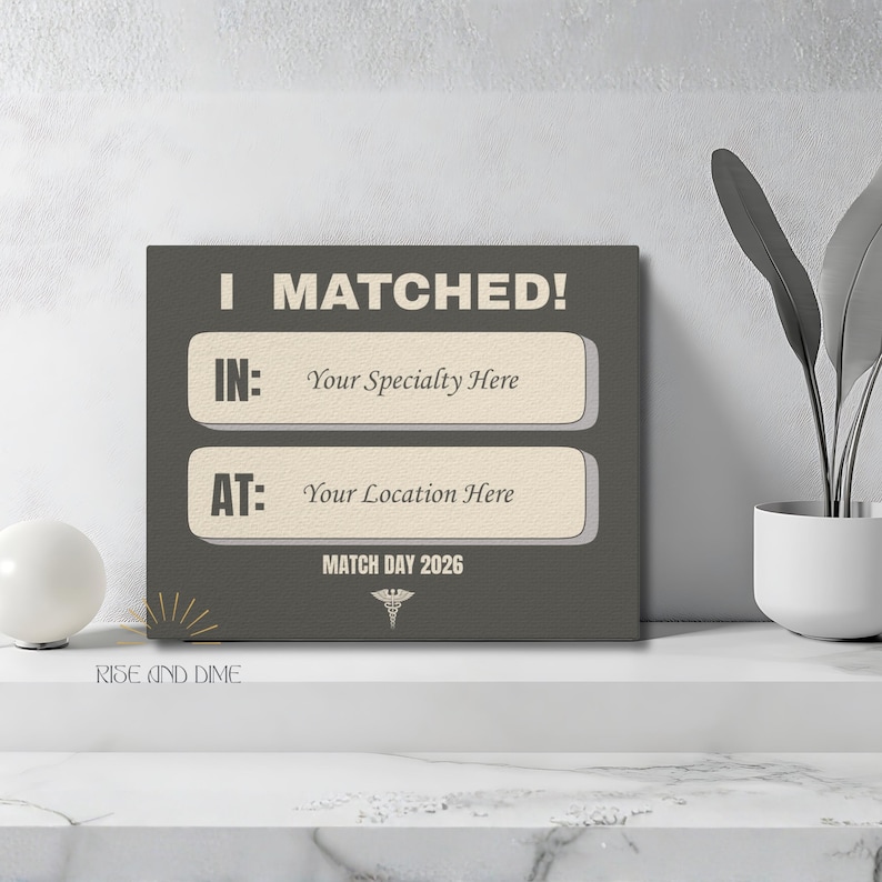 K&ouml;nnte beinhalten: Ein quadratischer Leinwanddruck mit dem wei&szlig;en Text "I MATCHED!". Darunter stehen in zwei rechteckigen Feldern "IN: Your Specialty Here" und "AT: Your Location Here". Der untere Text lautet "MATCH DAY 2026". Die Leinwand ist grau.
